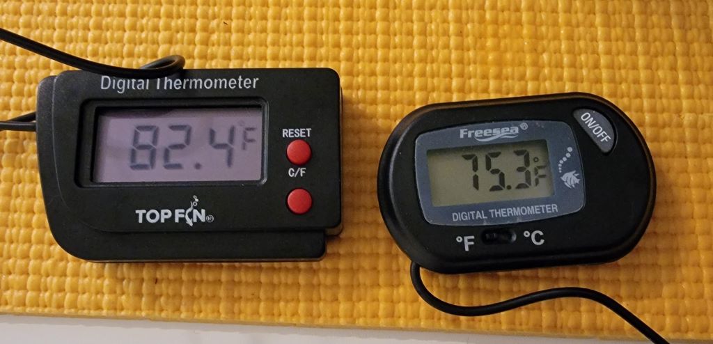 A close-up of a digital thermometer in a reef tank displaying a stable temperature of 77°F