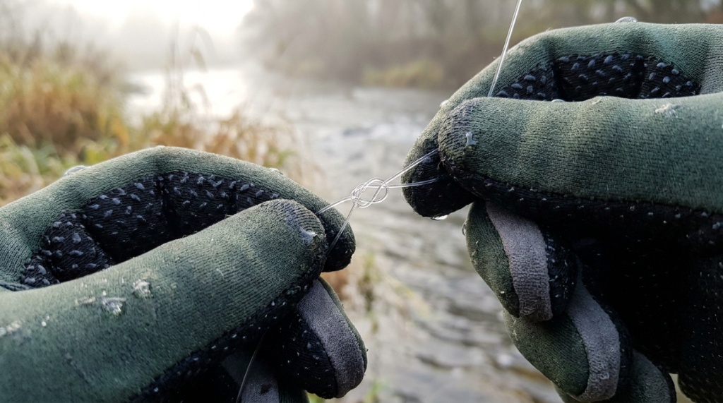 Close-up of textured non-slip fishing gloves tying a fishing line.